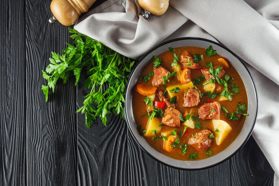 Готовый бограч в тёмной миске: кубики говядины, картофель, морковь и зелень