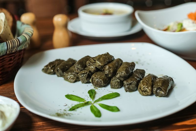 Готовая долма выложена рядами на белой тарелке, рядом соус