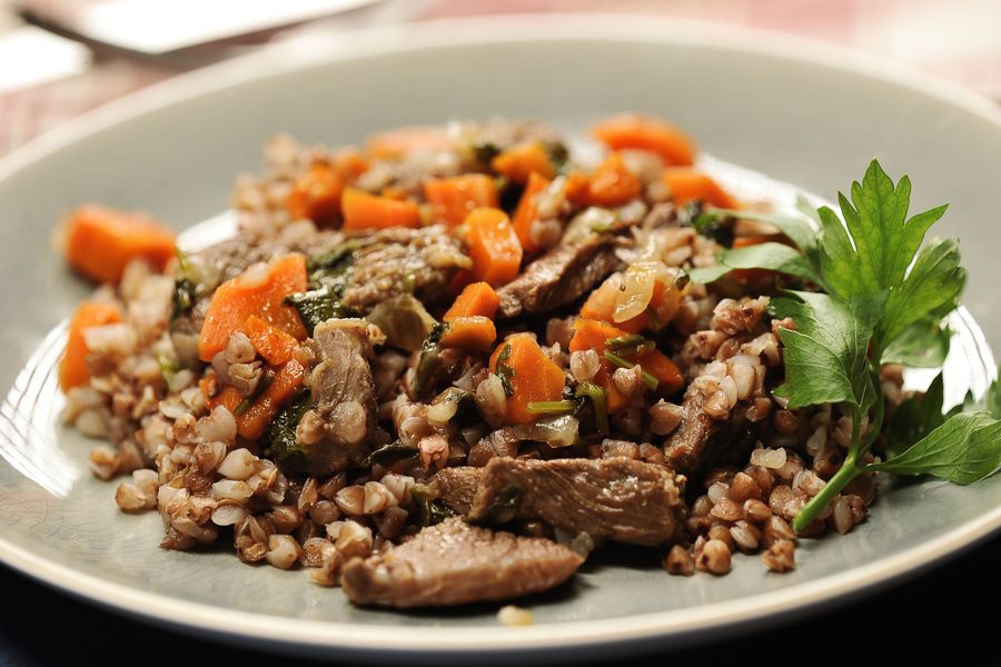 Гречневая каша с кусочками тушёного мяса и морковью на серой тарелке