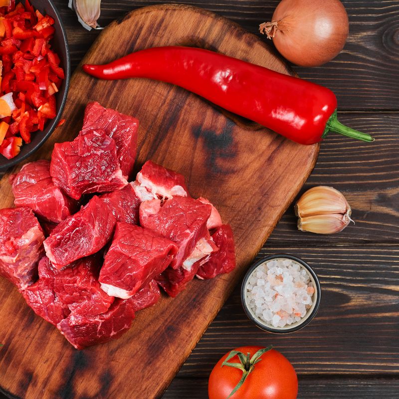 Куски сырой говядины на деревянной доске рядом с луком и крупной солью