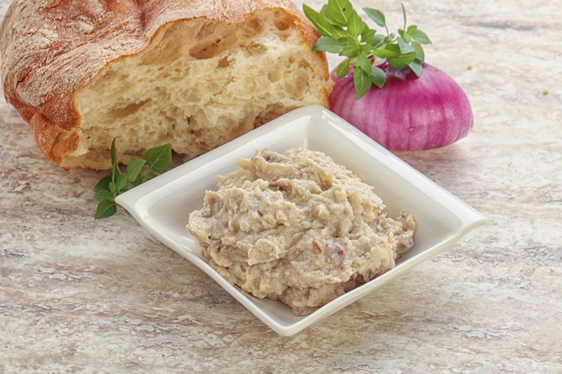 Форшмак после мясорубки в белой квадратной миске рядом с хлебом и луком