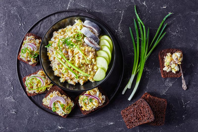 Рубленый форшмак с яйцом, яблоком и зелёным луком в чёрной миске и на ржаных тостах