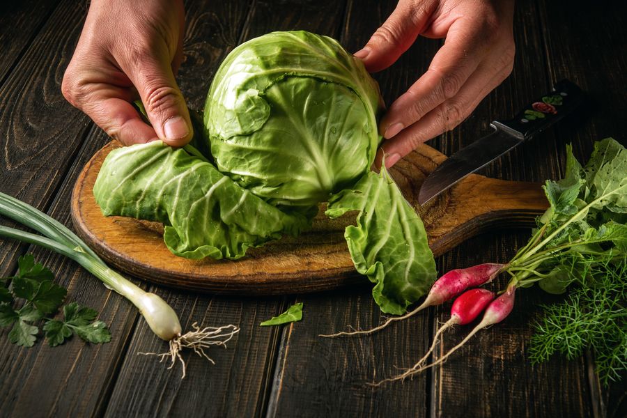 Руки отделяют лист от кочана белокочанной капусты на деревянной доске