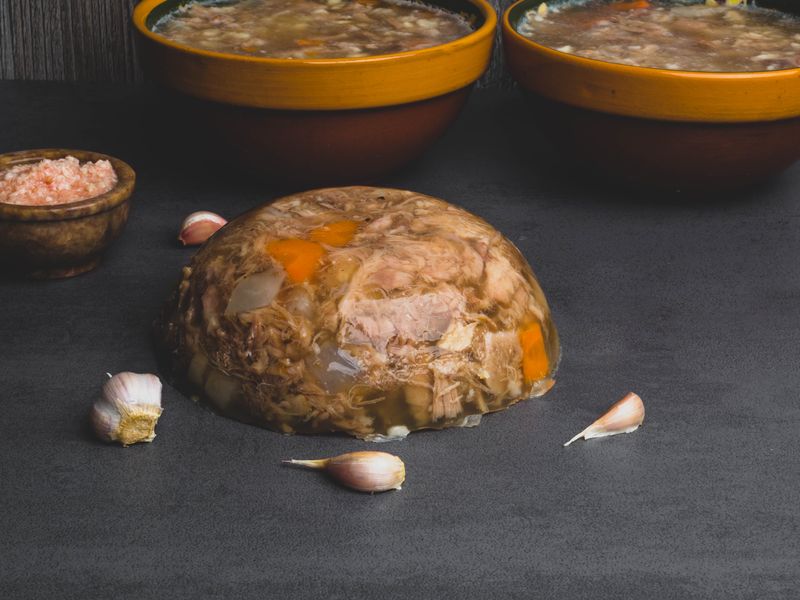 Застывший холодец, вынутый из формы куполом, рядом зубчики чеснока