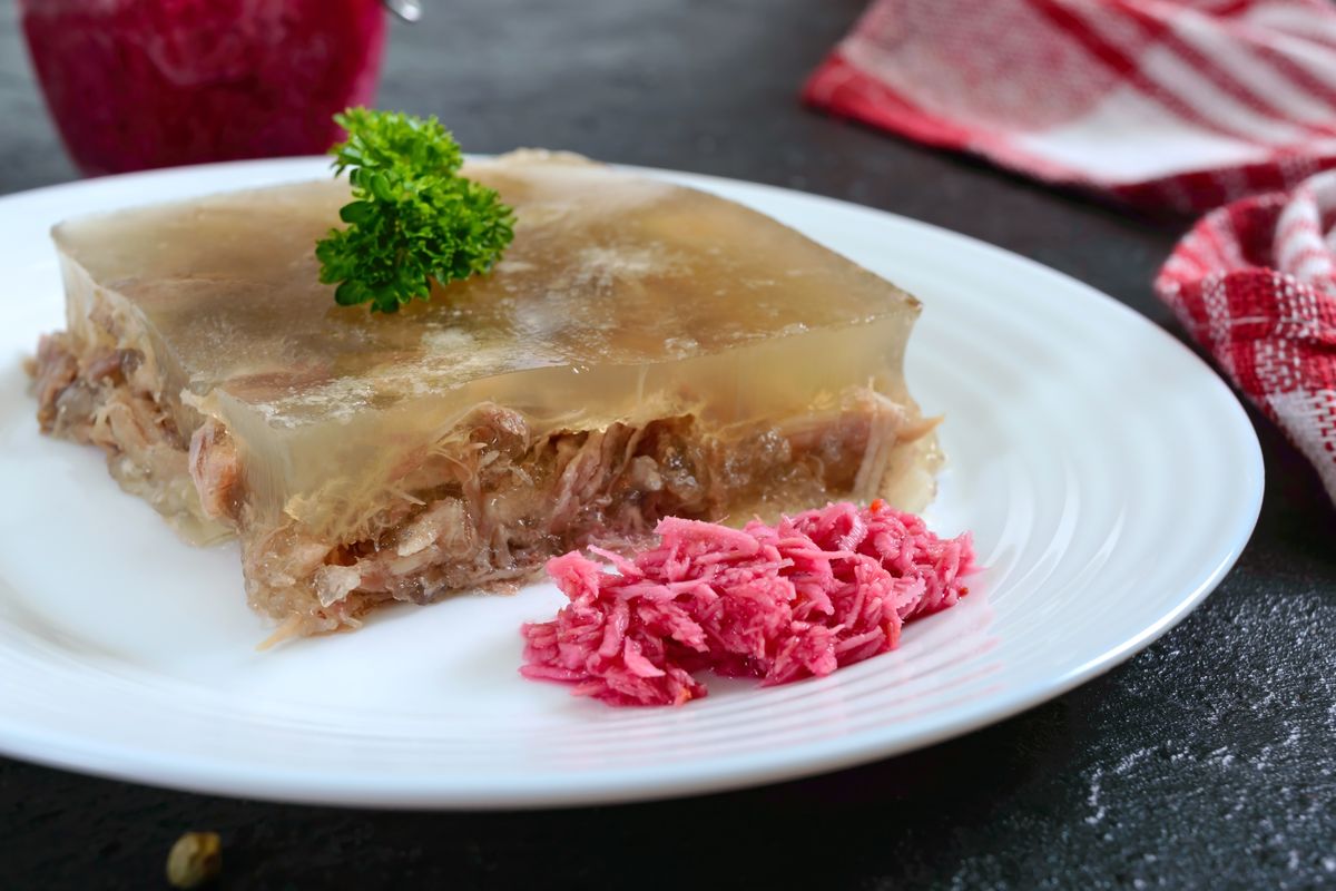 Кусок прозрачного холодца с мясом на белой тарелке с горкой красного хрена со свёклой
