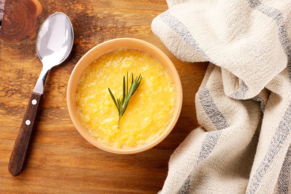 Густая жёлтая каша из кукурузной крупы в керамической миске с веточкой розмарина