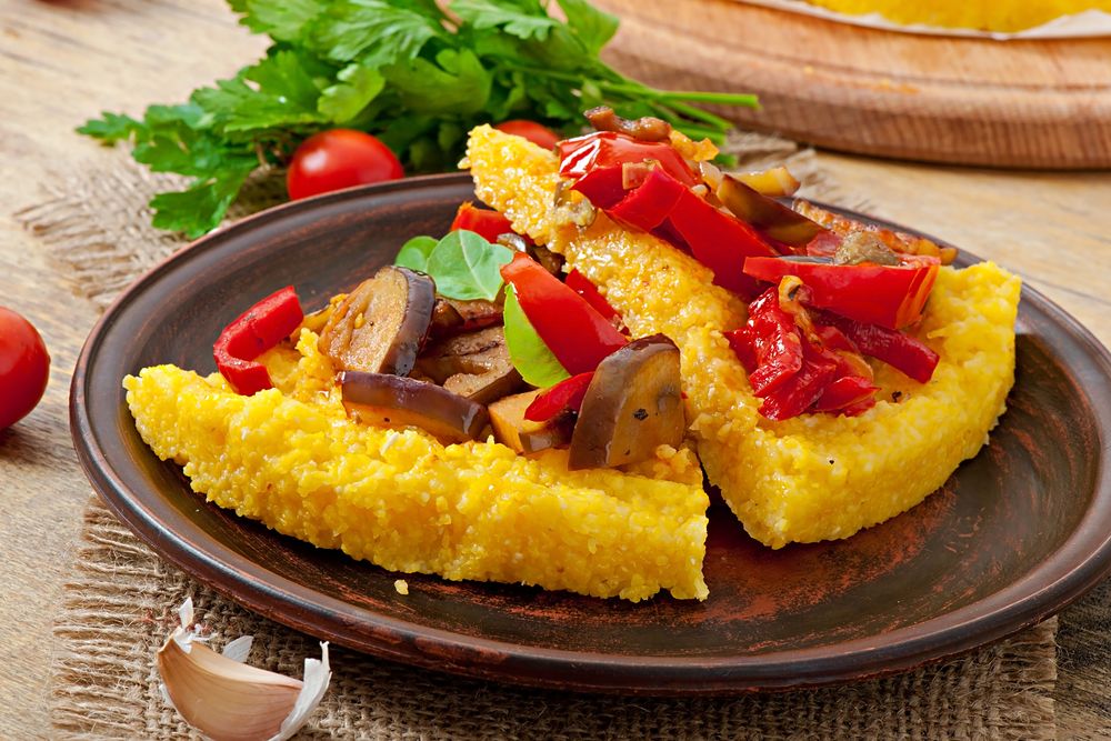 Ломти застывшей кукурузной каши, запечённые с перцем и баклажанами, на глиняной тарелке