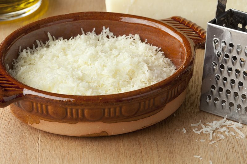 Тёртый пекорино в глиняной миске рядом с куском сыра и тёркой