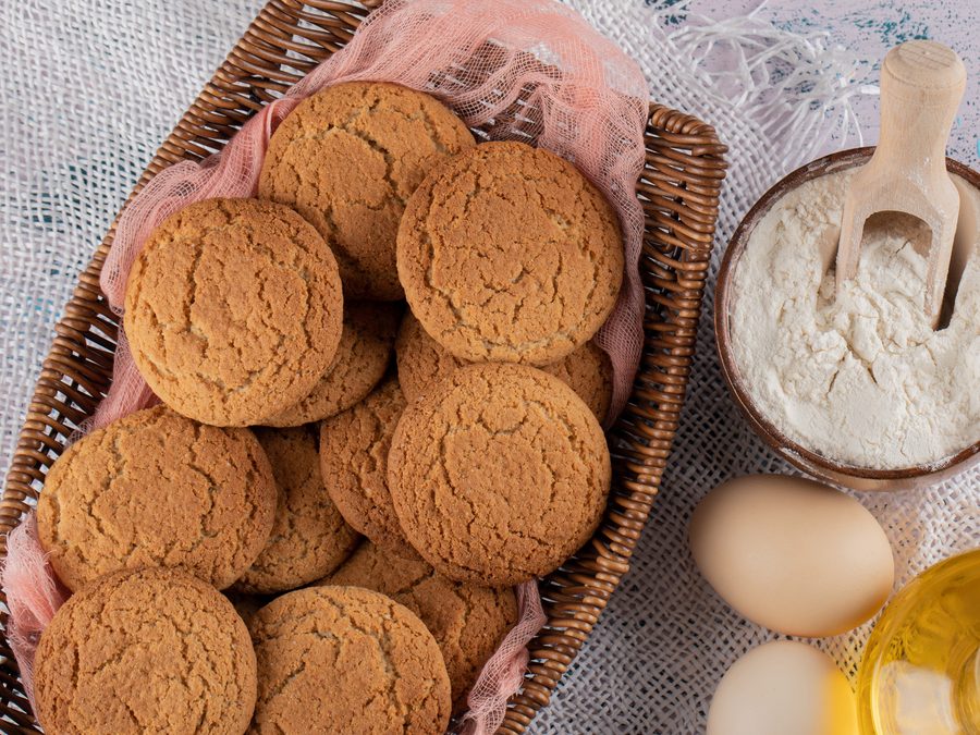 Корзина с овсяным печеньем, миска муки, два яйца и графин масла на столе