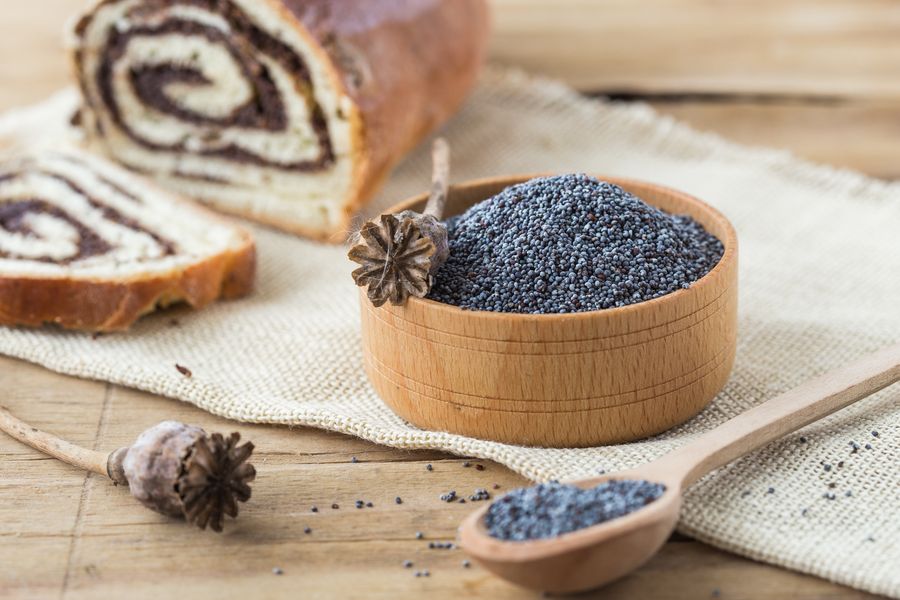 Блакитний мак у дерев'яній мисці, ложка маку і маковий рулет на лляній серветці