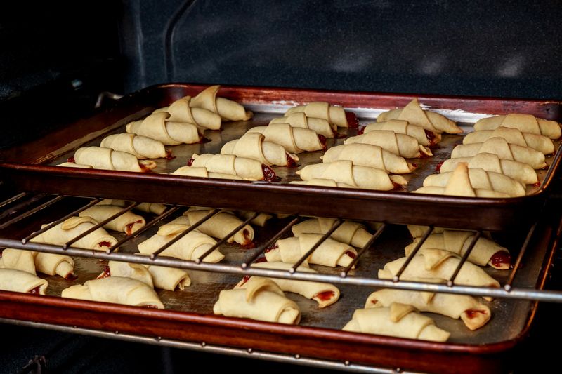Противни с рогаликами в духовке, из торцов видна красная начинка