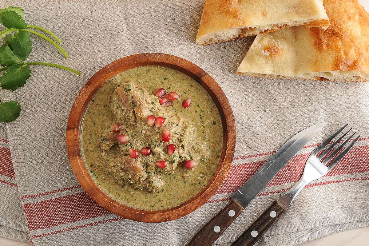 Сациви из курицы в деревянной миске, посыпанное зёрнами граната, рядом кинза и грузинский хлеб