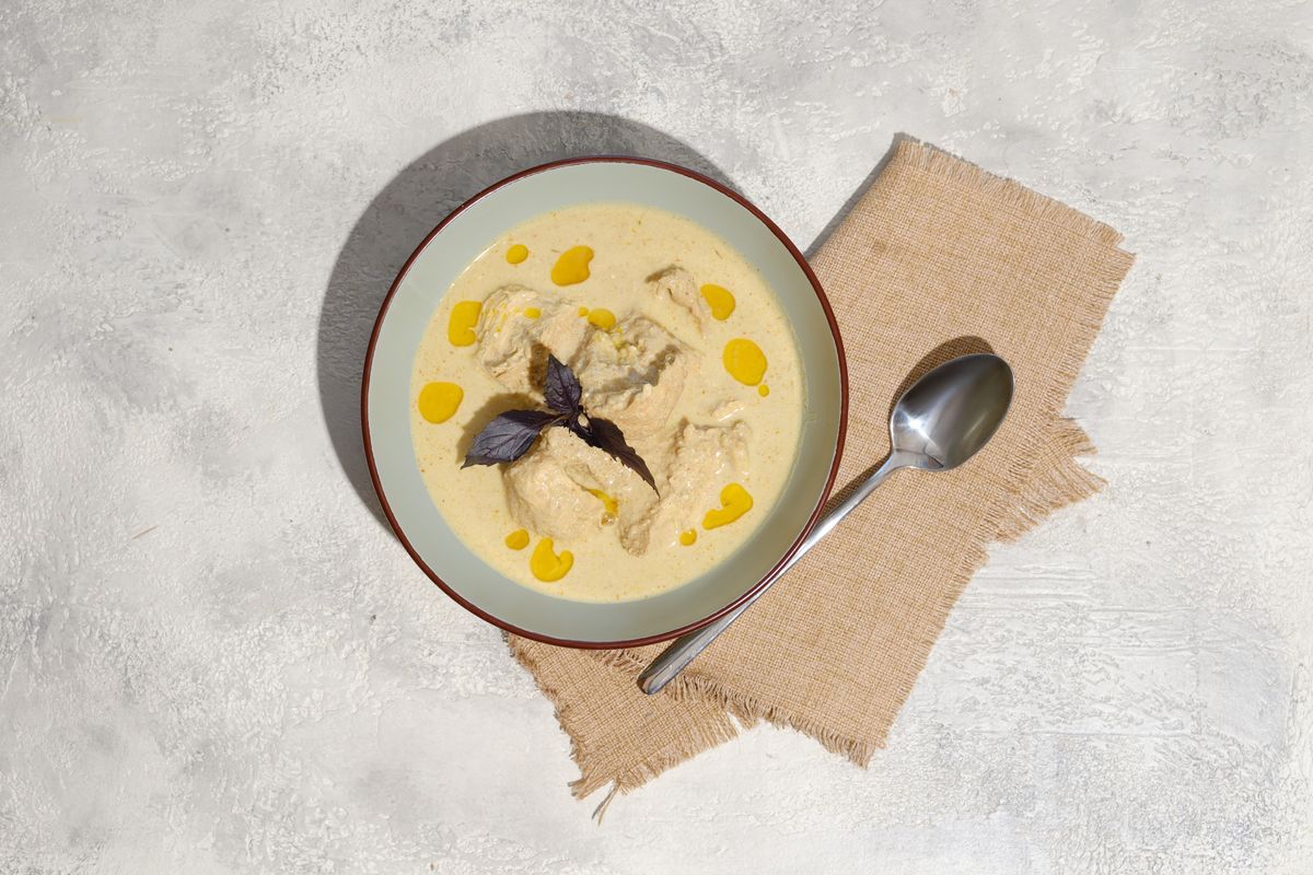 Сациви из курицы в глубокой тарелке на льняной салфетке, сверху капли орехового масла и лист базилика, рядом ложка