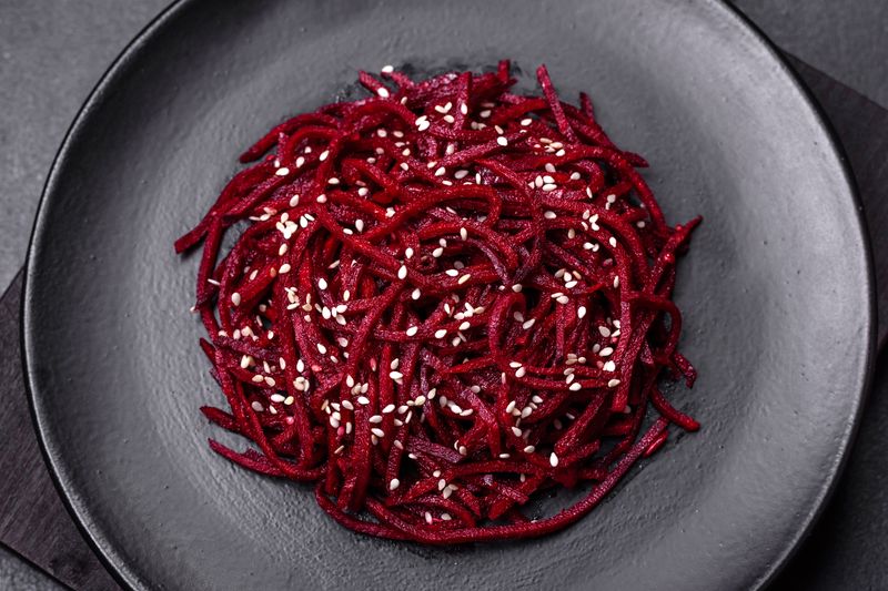 Свёкла по-корейски длинной соломкой с кунжутом на тёмной тарелке