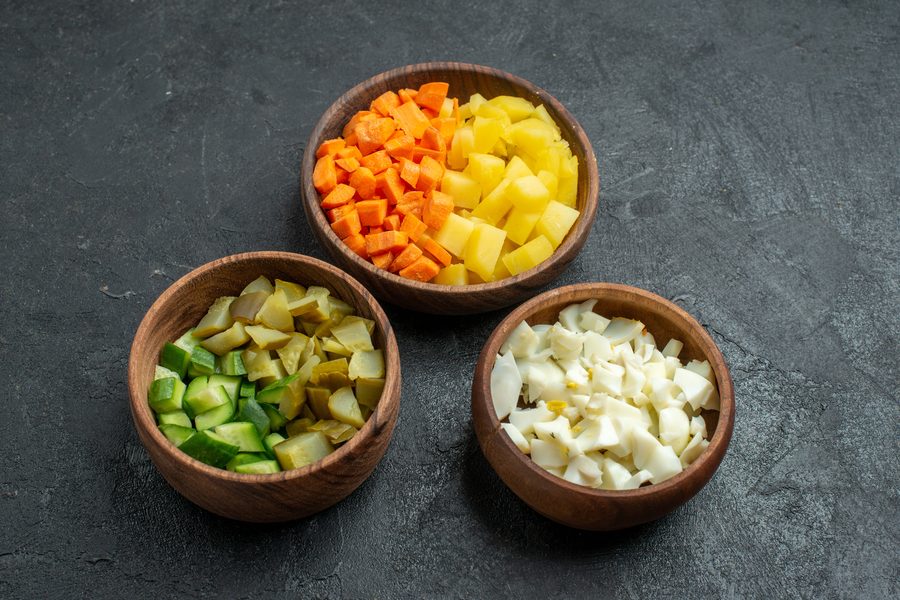Нарезанные кубиком картофель, морковь, огурцы и яйца в отдельных мисках
