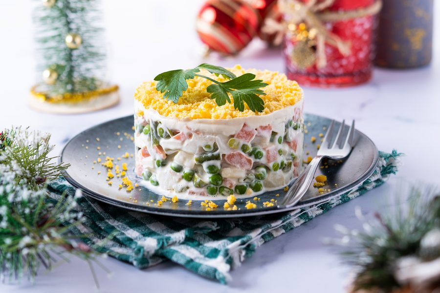 Порционный оливье, выложенный кольцом на тарелке, украшен зеленью