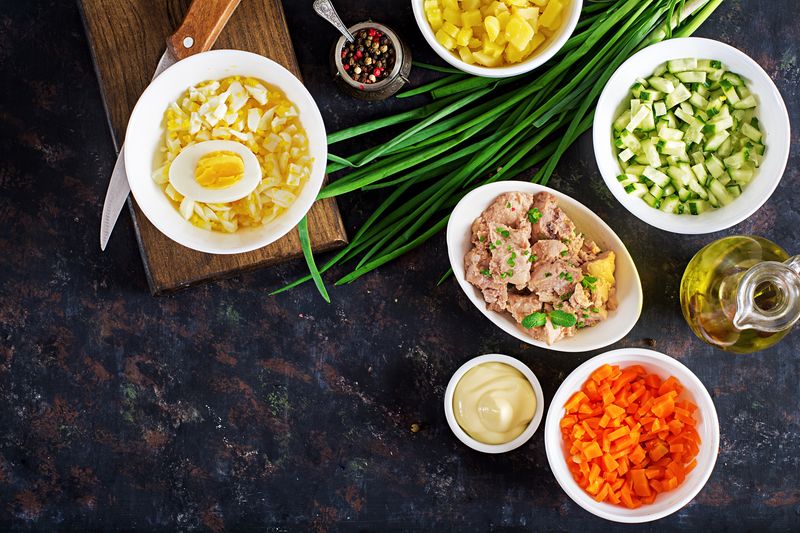 Нарезанные кубиком картофель, морковь, огурец, яйца и печень трески в отдельных мисках