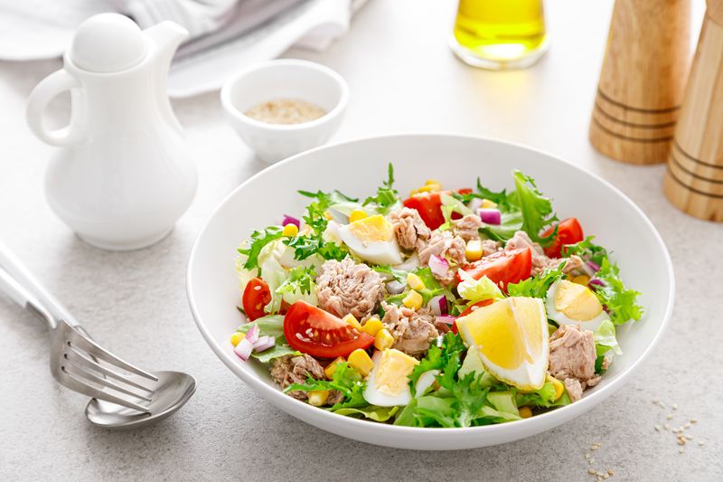 Салат с тунцом, яйцом, помидорами и кукурузой с долькой лимона в белой миске