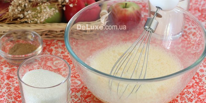 Яєчна маса збивається міксером, поряд склянка цукру