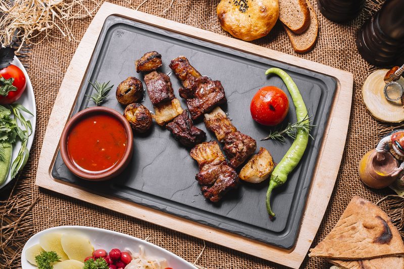 Жареное мясо с картофелем на каменной доске и красный соус в глиняной миске
