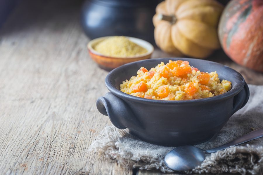 Пшённая каша с кубиками тыквы в тёмной керамической миске, рядом миска с пшеном
