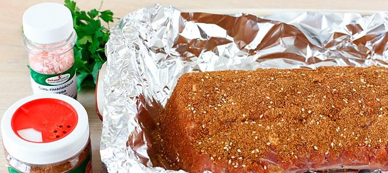 Свинина натёртая мясной приправой лежит на развёрнутой фольге в форме