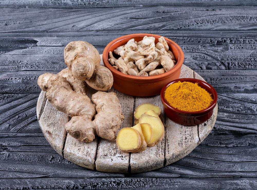 Свежий корень имбиря, миска сушёных кусочков и миска молотого имбиря