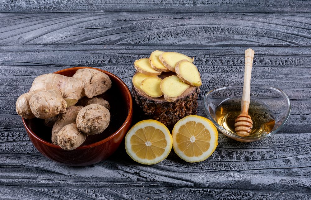 Корни имбиря в миске, нарезанные ломтики, половинки лимона и мёд
