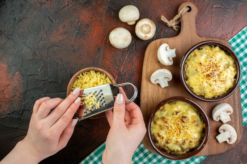 Тёртый сыр натирают на мелкой тёрке над горшочками с жульеном