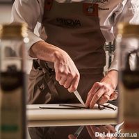 Повар в фартуке Prova Gourmet разрезает стручок ванили на доске